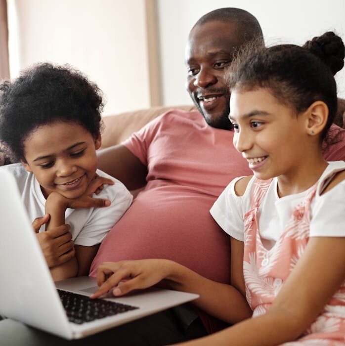 Smiling father and kids using a laptop at home, sharing joyful moments.